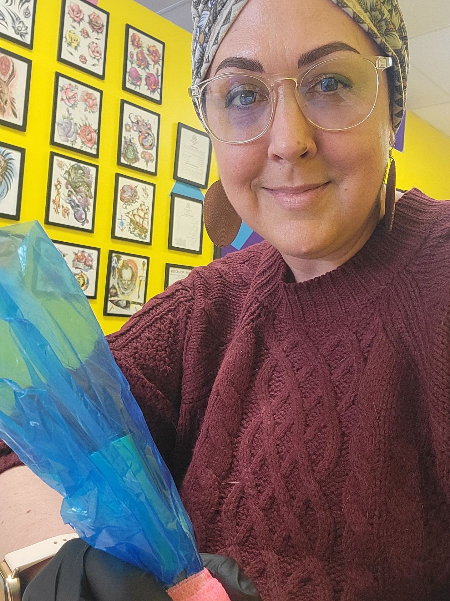 Person holding a colorful object against a backdrop of framed artwork on a bright yellow wall.